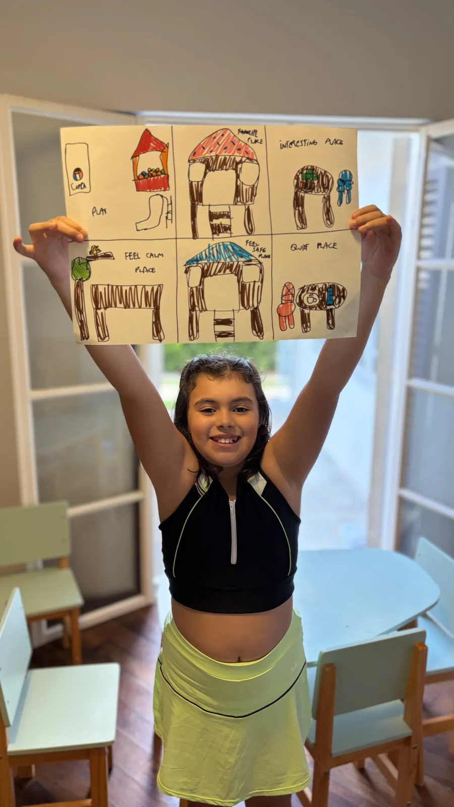 Criança erguendo uma cartela com desenhos dos seus lugares favoritos, escritos em inglês